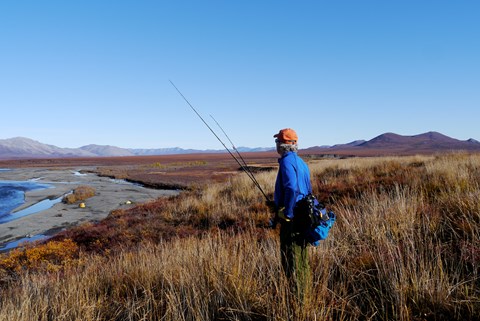 Man standing with fishing pole on tundra, water in the background