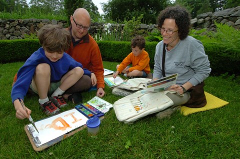 A family sitting in the grass painting.