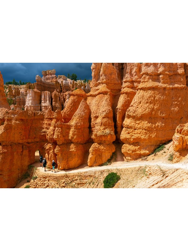 Hikers walk along a trail towards an open archway in the red rock