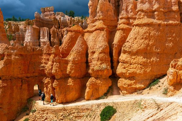Hikers walk along a trail towards an open archway in the red rock