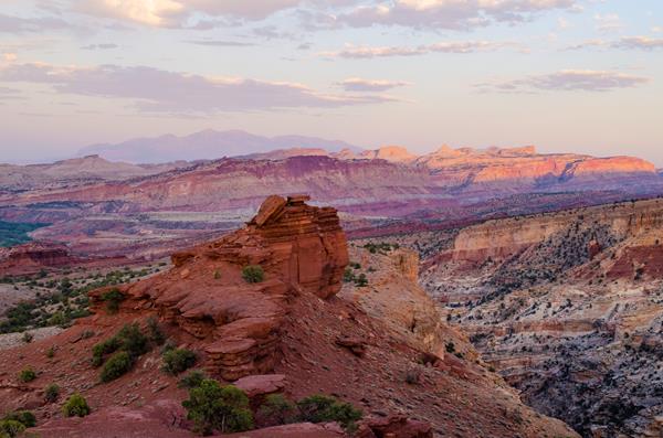 Colorful red rocks, striped cliffs, mountains in the distance, and a pale blue moving to purple sky.