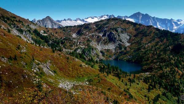 A small blue subalpine lake surrounded by meadows, with mountains behind.