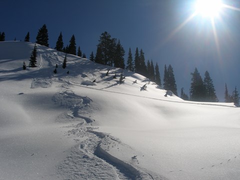 A skier heads downhill on a steep snow-covered slope.