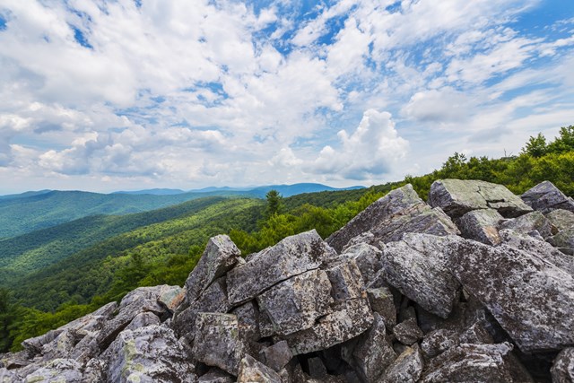 A jumble of large boulders sits on a cliff over a view of the valley below.