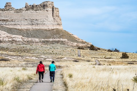 Two hikers walk towards an interesting rock formation.
