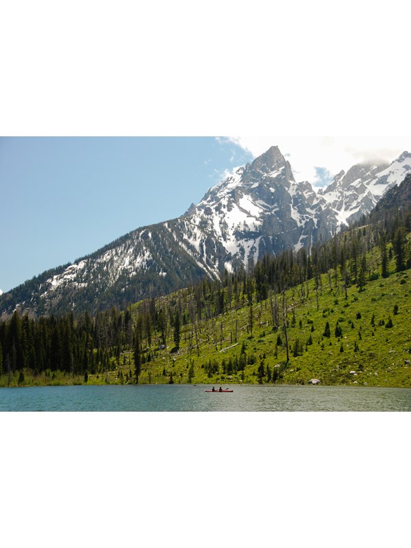 A kayak floats in a turquoise lake at the base of jagged mountain peaks.