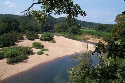 view from above of trees and river at right and tan gravel and trees at left.