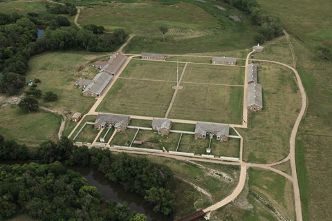 Aerial view of sandstone buildings arranged in a square around an open grassy area.