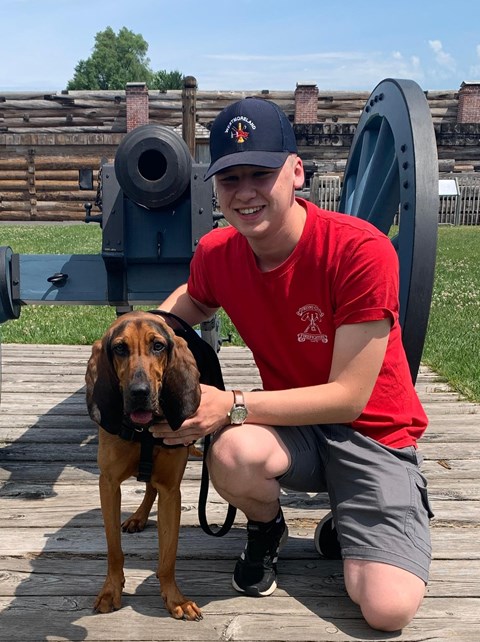 A sweet doggy stands on a leash with his person in front of a cannon.