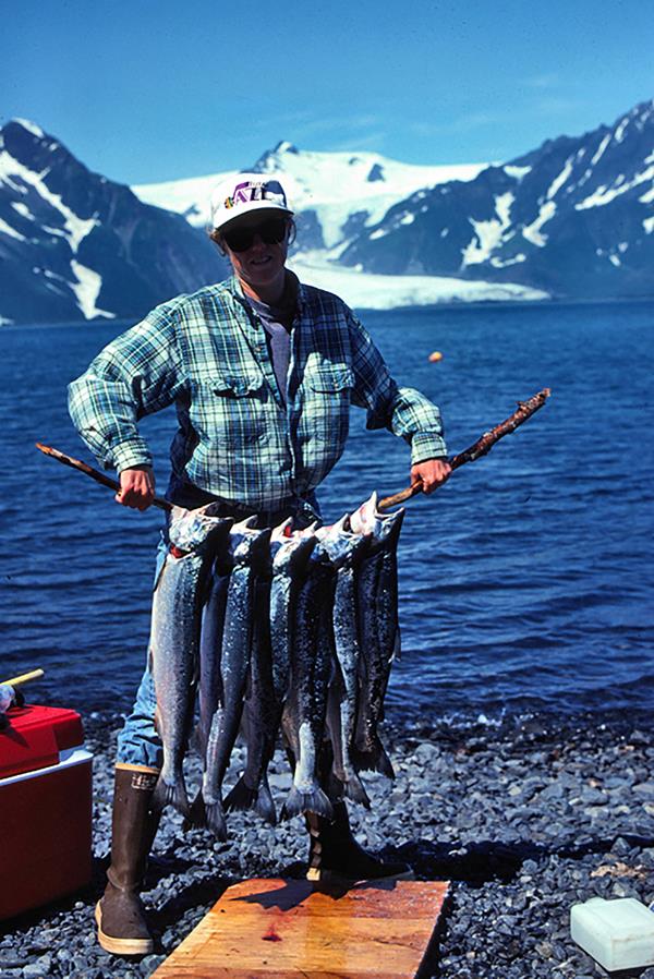 A man holding a stick with six salmon hanging from the stick.