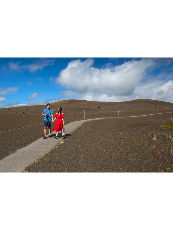 Two people holding hands on a paved path through a cinder-covered landscape