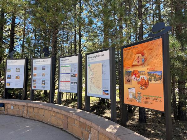 Five informational signs stand side by side behind a curved stone wall.