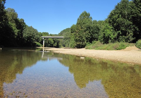 water in foreground with tan gravel at right and highway bridge in background