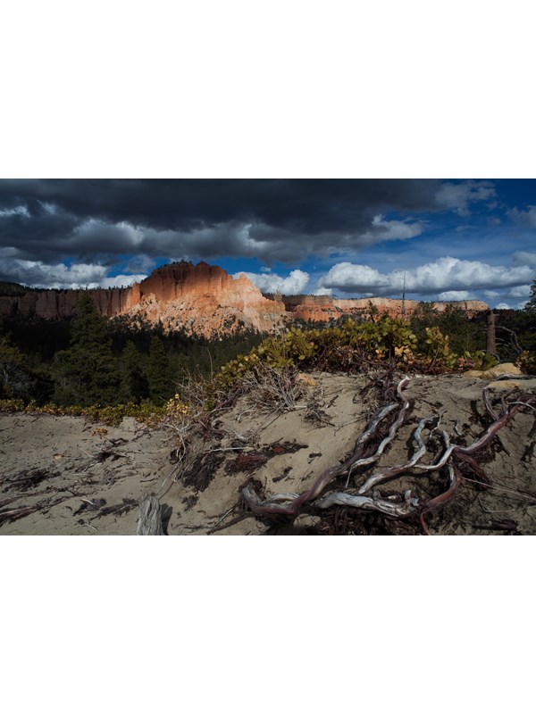 A large formation of red rock partially in shadow with threatening storm clouds above it