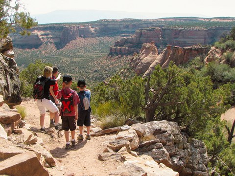 two adults and two children stand on dirt path looking out towards wide open canyons