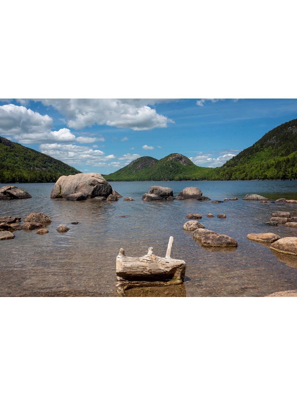 The placid surface Jordan Pond with exposed boulders and a log protruding from the water.