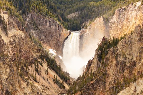 A 300 foot waterfall spills into a canyon colored in shades of yellow and gray.