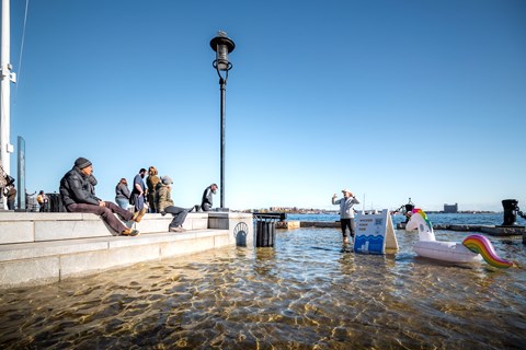 People sitting on Long Wharf as someone in wellies stands in the flooded lower area of the walkway.