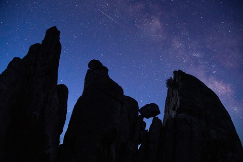 Silhouettes of 3 large pinnacles and a smaller balanced boulder under a purple and blue starry sky.