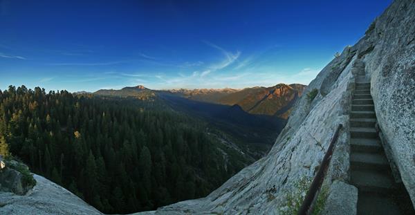Stone stairs climb a granite peak next to an expansive view of a valley and mountain peaks