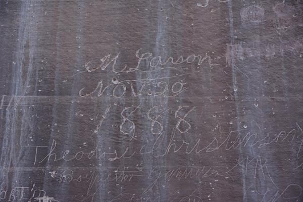 signatures carved into reddish rock wall.