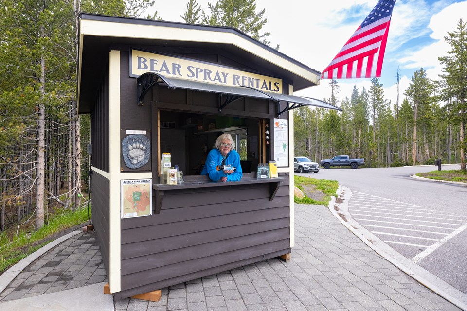 An employee leans out the window of a bear spray rental kiosk with a can of bear spray.
