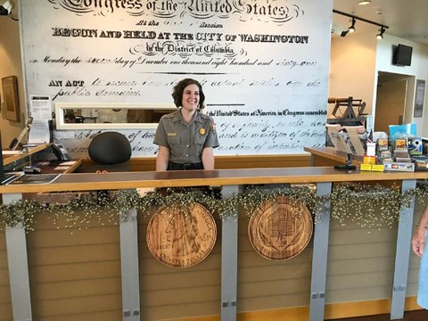 A ranger smiles standing behind an information desk.
