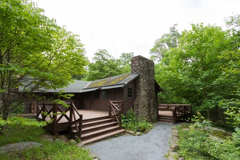 An historic cabin with a large porch sits in the middle of a forest.