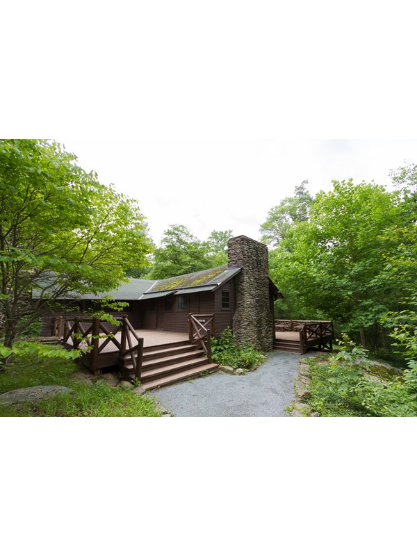 An historic cabin with a large porch sits in the middle of a forest.
