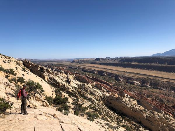 A hiker stands on top of rock cliff viewing vast valley below.