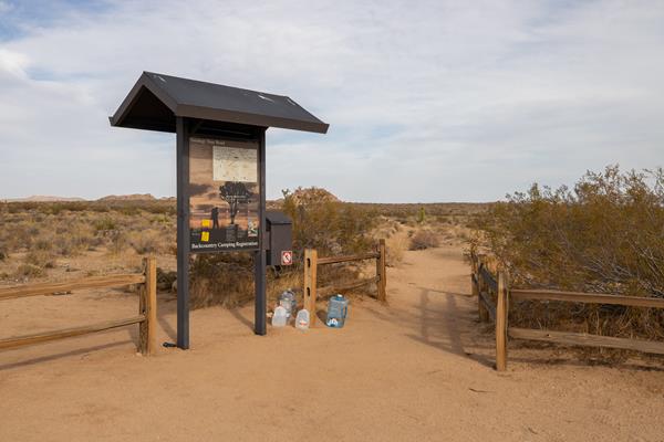 An information board next to a trailhead with a short wooden fence.