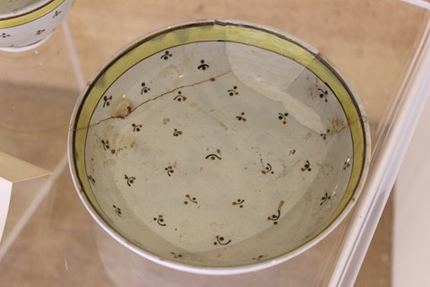 A white ceramic saucer with a small decorative design and yellow rim.