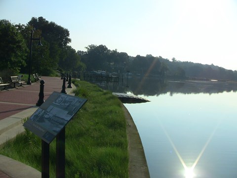 a curving concrete pathway and green border along water with a sloping kayak launch