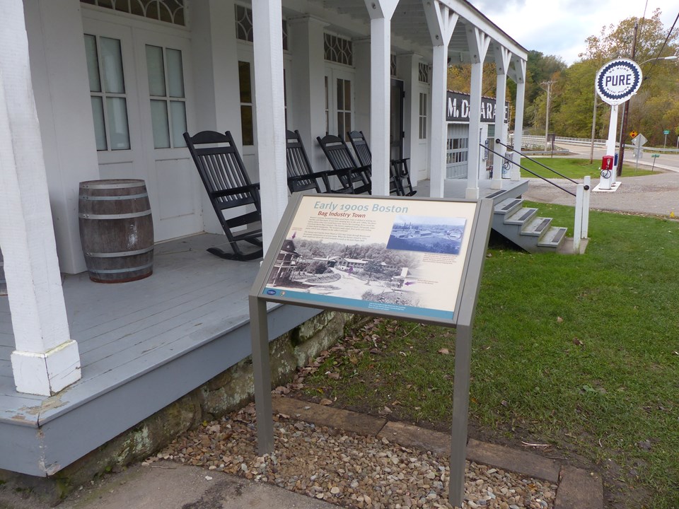 Graphic panel beside a white historic building's porch; rocking chairs and a barrel on the porch.