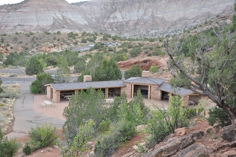 Stone structure with open walls covering picnic tables, in an open area surrounded by canyon walls