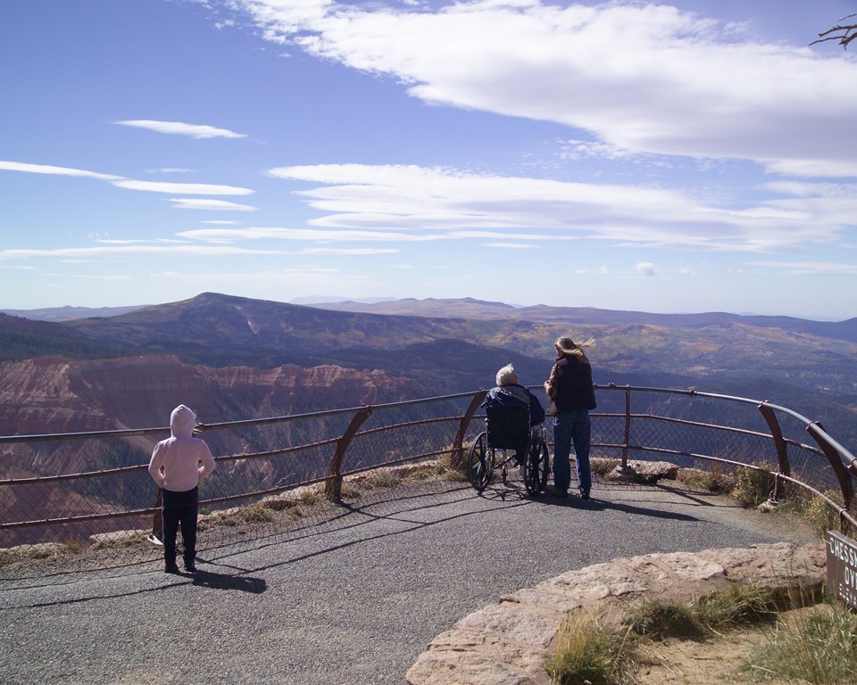 Three people look over railings to rock formations in the distance.