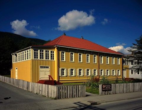Two-story historic building with yellow walls and red metal roof.