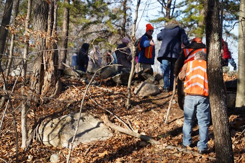 People walking up hill. Some wearing orange safety vests