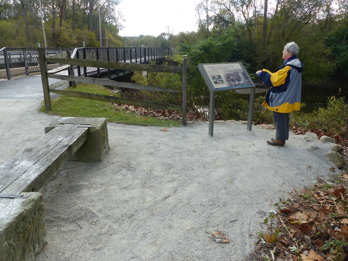 A woman in a raincoat reads a graphic panel by a stream.