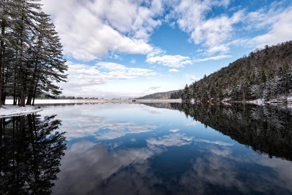 A winter scene of a lake framed by snowy trees on the left and a mountain ridge on the right.