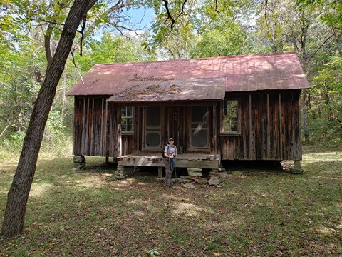 an old cabin with weathered brown wood siding running up and down, tin roof rusted and ranger
