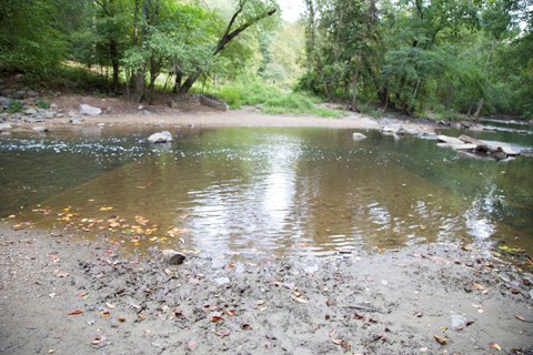 A road is barely visible beneath the brown still waters of the creek