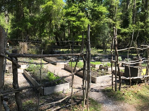 Split-rail fence surrounding a garden area with raised plant beds and trees in the background.