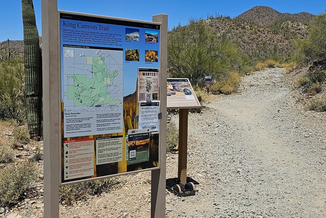 Large trailhead sign with a map and information beside a trail that curves to the right
