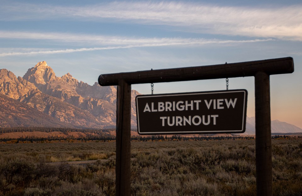A wooden sign that reads albright view turnout with the teton range and sagebrush in the background.