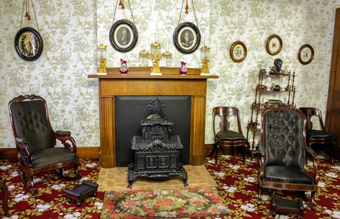 Black iron stove set in fireplace, flanked by black cushioned rockers. Framed images adorn walls.