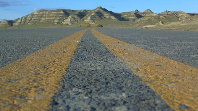 Road level view of a paved road with two yellow center lines curving toward distant buttes