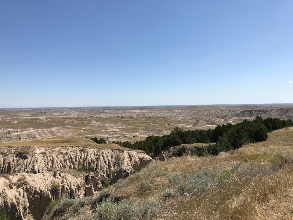 an expansive basin of mixed-grass prairie and badlands formations beneath blue sky.