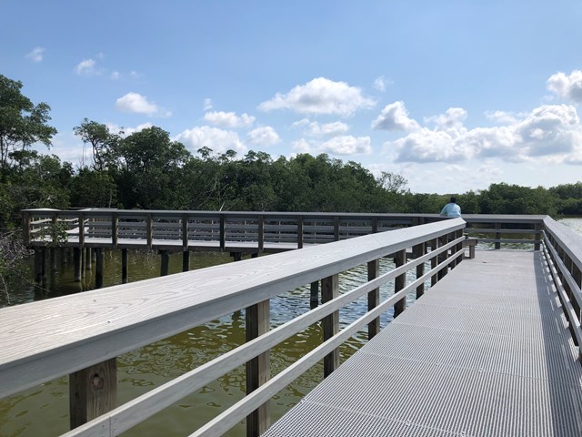 Gray boardwalk extending toward the horizon with a person fishing off the edge into the water