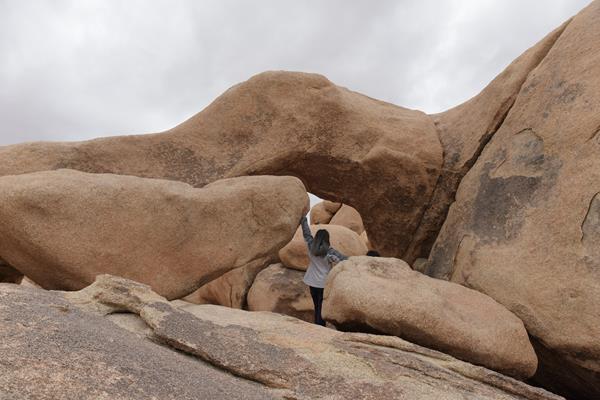 A hiker walking along a barren trail with desert vegetation and small boulders.